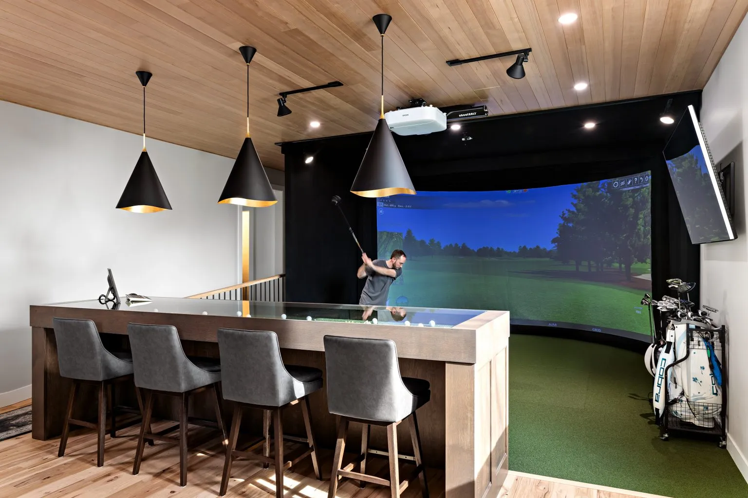 Residential golf simulator room with bar seating and projection screen